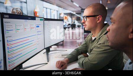 Two Young Professionals Collaborate On Business Goals Using Software Dashboard. Stock Photo