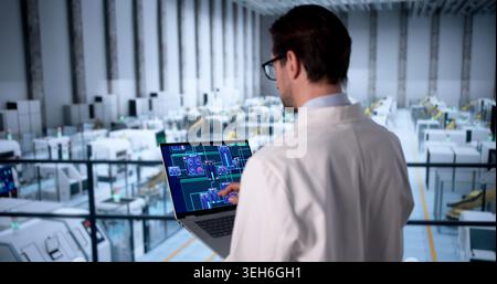 Experienced Man In Uniform Inspects Factory Machinery Using Laptop For Safety. Stock Photo