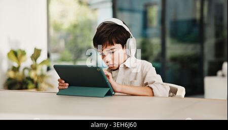 E learning, headphones and child in home with tablet, online activity or project on academic app. Homeschool, tech and boy in kitchen with homework Stock Photo