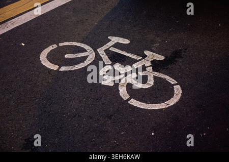 White Bicycle Lane Symbol Painted on Dark Asphalt Road Surface at Night Stock Photo