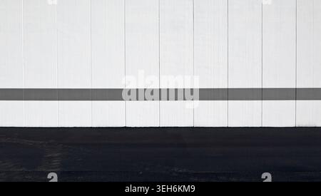 White concrete wall made of vertical blocks with a gray painted horizontal line. Street in front. Background for copy space. Stock Photo