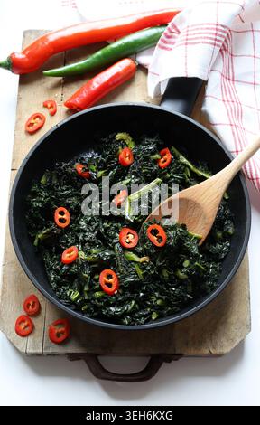 Healthy side dish of sautéed tuscan kale cooked in a pan with olive oil and sliced fresh red chili. Overhead view. Stock Photo