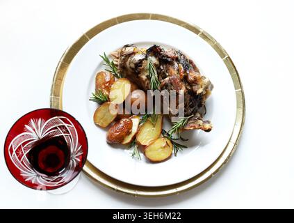 Delicious roasted leg of lamb served with crispy rosemary potatoes and a glass of red wine on an elegant table setting. Christmas and holiday season. Stock Photo