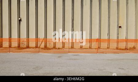 Safety temporary orange plastic netting fence for construction industry in front of a large concrete block wall. Background and texture. Copy space. Stock Photo
