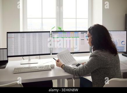 Accountant analyzing financial data on multi monitor workstation in modern office Stock Photo