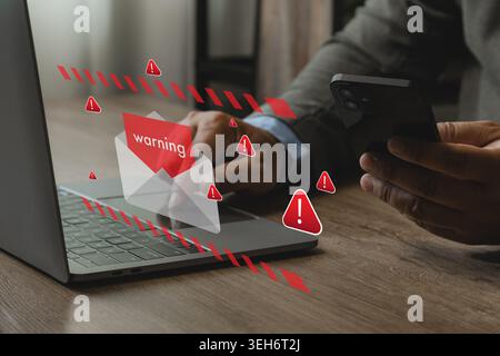 Person holding smartphone near laptop with phishing email warning icons and spam alert interface, representing cyber security risk, fake text message Stock Photo