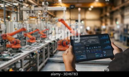 Engineer using tablet dashboard in smart factory with robotic automation system for industrial production monitoring, manufacturing analytics, and ope Stock Photo