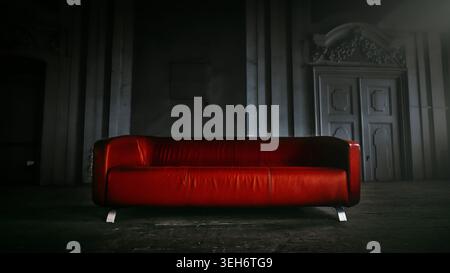 Modern red leather sofa in dark atmospheric abandoned room with dramatic spotlight. Minimalist luxury couch in moody rustic architectural hall. Stock Photo