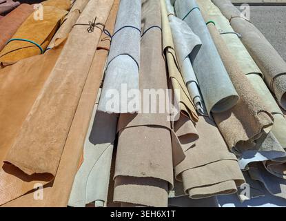 Rolled leather and suede skins in colors like beige, tan, and light grey are arranged side by side at a market. The texture and variety showcase the m Stock Photo