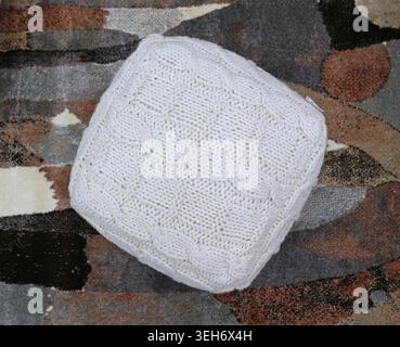 Square woolen white pouf on multicolored carpet background. Top view. Stock Photo