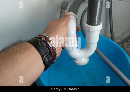 Hand fixing a leaking P-trap pipe under kitchen sink with water in bucket Stock Photo