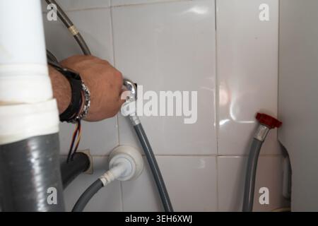 Plumber connecting a washing machine water hose to a valve in a utility room Stock Photo