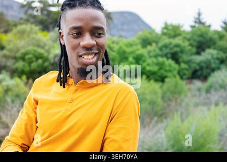 African American man sitting at park wearing mustard yellow henley, looking right and smiling Stock Photo