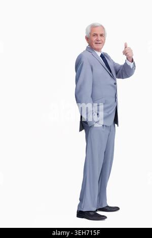 Senior man standing in studio wearing light gray suit and dark tie, giving thumbs-up, copy space Stock Photo