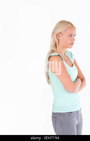 Woman standing arms crossed, facing right in white studio, wearing mint top, gray jeans, copy space Stock Photo