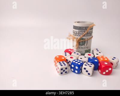 A rolled stack of United States dollar bills secured with twine sits next to a pile of multicolored dice. Stock Photo