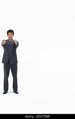 Asian man posing left in studio giving two thumbs-up, wearing suit, necktie, copy space Stock Photo