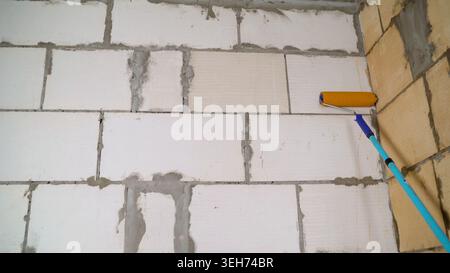 Close up of priming process on unfinished concrete block wall. Yellow roller applies beige coating. DIY home renovation and construction background. N Stock Photo