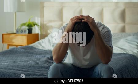 Worried tired Caucasian man sitting bed home holding head stressed male in bedroom exhausted anxious guy headache pain problems crisis trouble Stock Photo