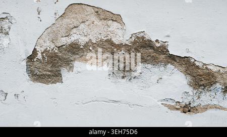 A close up shot of a weathered concrete wall where the grey paint is peeling away to reveal the rough. Stock Photo