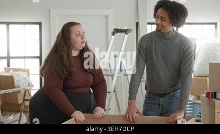 Man and woman packing cardboard boxes, hands on box and holding picture frame while moving into building; moving day love. Stock Photo