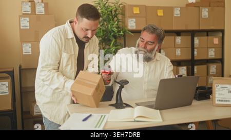 Two men scan and pack a cardboard box with hands visible, one holds a barcode scanner while the other places the parcel on a desk in a building; focus Stock Photo