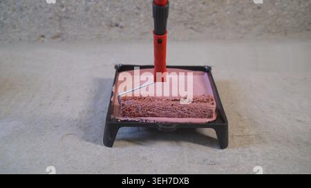 Paint roller in a paint tray. The primer is pink. Pink paint in a tray with a roller. Stock Photo