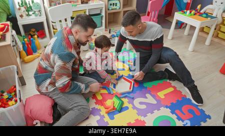 Man and boy placing wooden block into hexagon puzzle on foam number mat in a building playroom; playful bonding. Stock Photo