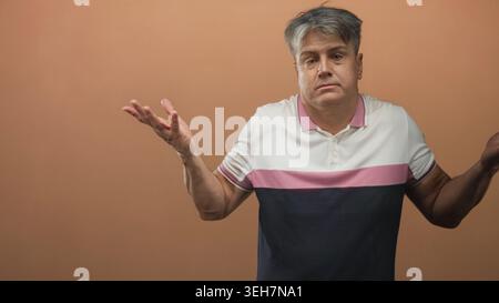Man pointing both index fingers with visible hands against studio backdrop wearing a polo shirt; contemplation introspection. Stock Photo