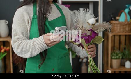 Woman florist holds smartphone in hand while arranging a purple calla lilies bouquet and pampas grass in a studio; calm focus. Stock Photo