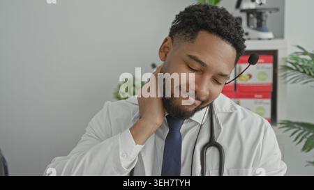 Man doctor with stethoscope rubs neck while adjusting headset in building during virtual consult; concern. Stock Photo