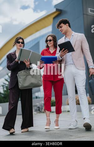 Business colleagues walking and discussing documents outside a modern office building, smiling professionals collaborating Stock Photo