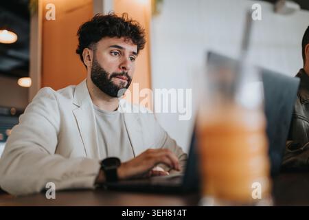 Focused man working on laptop in a cafe wearing a light blazer and casual shirt Stock Photo