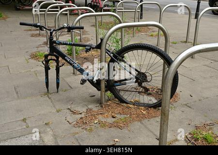 Partially stolen bicycle locked to rack on sidewalk beside city street today Stock Photo