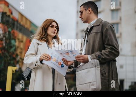 Business colleagues discussing printed charts outdoors during a casual meeting in an urban setting Stock Photo