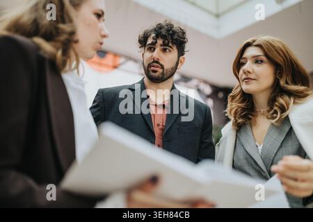 Three young professionals in a focused business meeting reviewing documents and discussing strategy Stock Photo