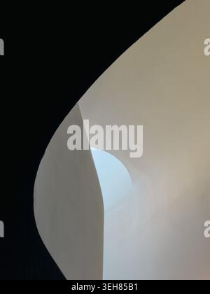 A smooth curved white architectural surface sweeps across the frame with a small arched opening revealing pale blue sky, set against deep shadow in a bold minimalist architectural composition. Stock Photo