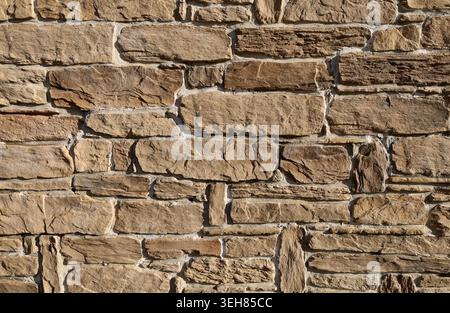 Stone wall made of brown natural rocks of different shapes and sizes on concrete. Background and texture. Stock Photo