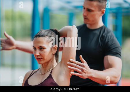 Female athlete stretching with personal trainer assisting at outdoor fitness park for strength and mobility Stock Photo