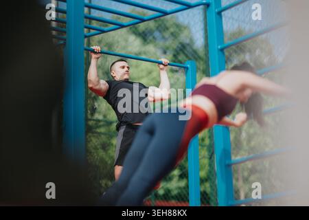 Man doing pull-up at outdoor gym while partner works on parallel bars in athletic workout Stock Photo