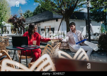 Business colleagues meeting outdoors at a cafe exchanging documents during a casual work discussion Stock Photo