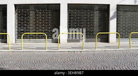 Closed shop with the folding security gates down. Sidewalk, yellow pedestrian barrier and porhyry road in front. Background for copy space Stock Photo