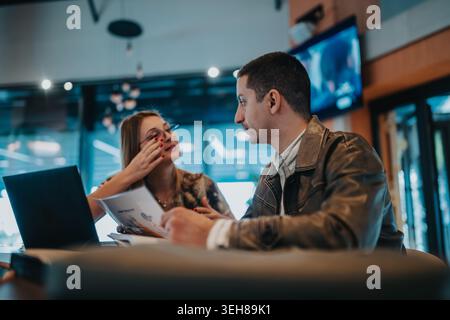 Two colleagues discussing documents over a laptop during a casual business meeting in a cafe Stock Photo