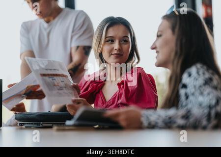Three friends discussing documents together at a casual table meeting in a bright office Stock Photo