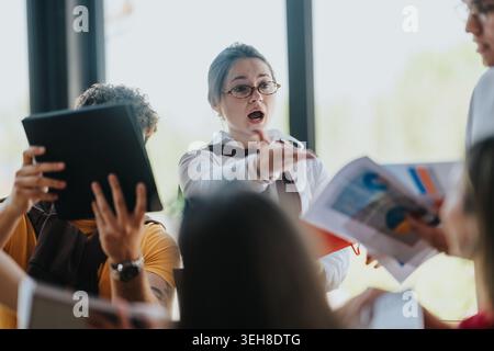 Friends debating documents in a lively group meeting with woman pointing and speaking emphatically Stock Photo