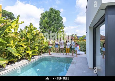 Group of diverse young adult friends smiling and socializing at a poolside gathering, enjoying drinks and conversation during a sunny summer vacation Stock Photo