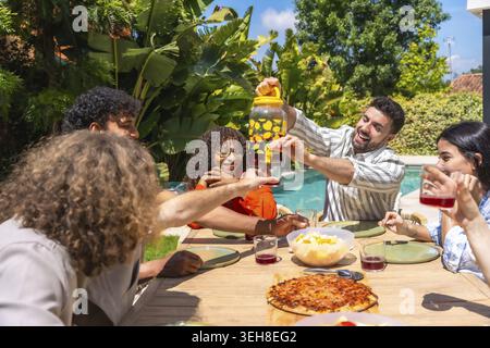 Diverse group of friends celebrating friendship and sharing food and drinks at a vibrant outdoor gathering with a refreshing beverage dispenser, enjoy Stock Photo