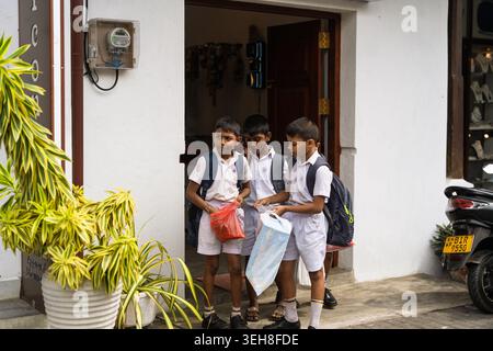 Sri Lanka - 07 January 2026: View of three schoolboys in white uniforms standing in a doorway of a white building with their school bags. Stock Photo