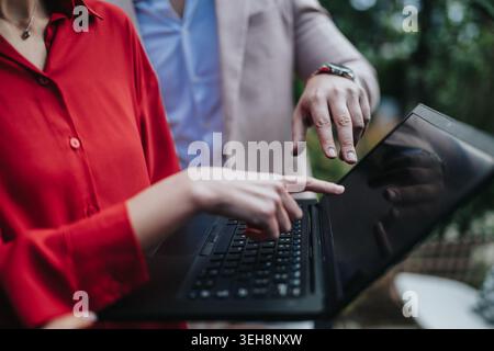 Two professionals collaborating over a laptop during an outdoor business discussion and review Stock Photo