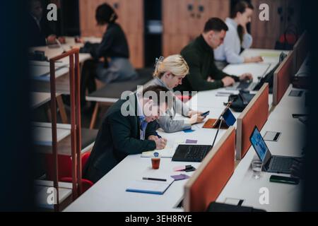 Business professionals working together in a modern co-working space taking notes and using laptops Stock Photo